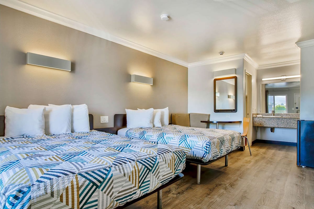 Quarto de hotel com duas camas, banheiro e cozinha compacta.