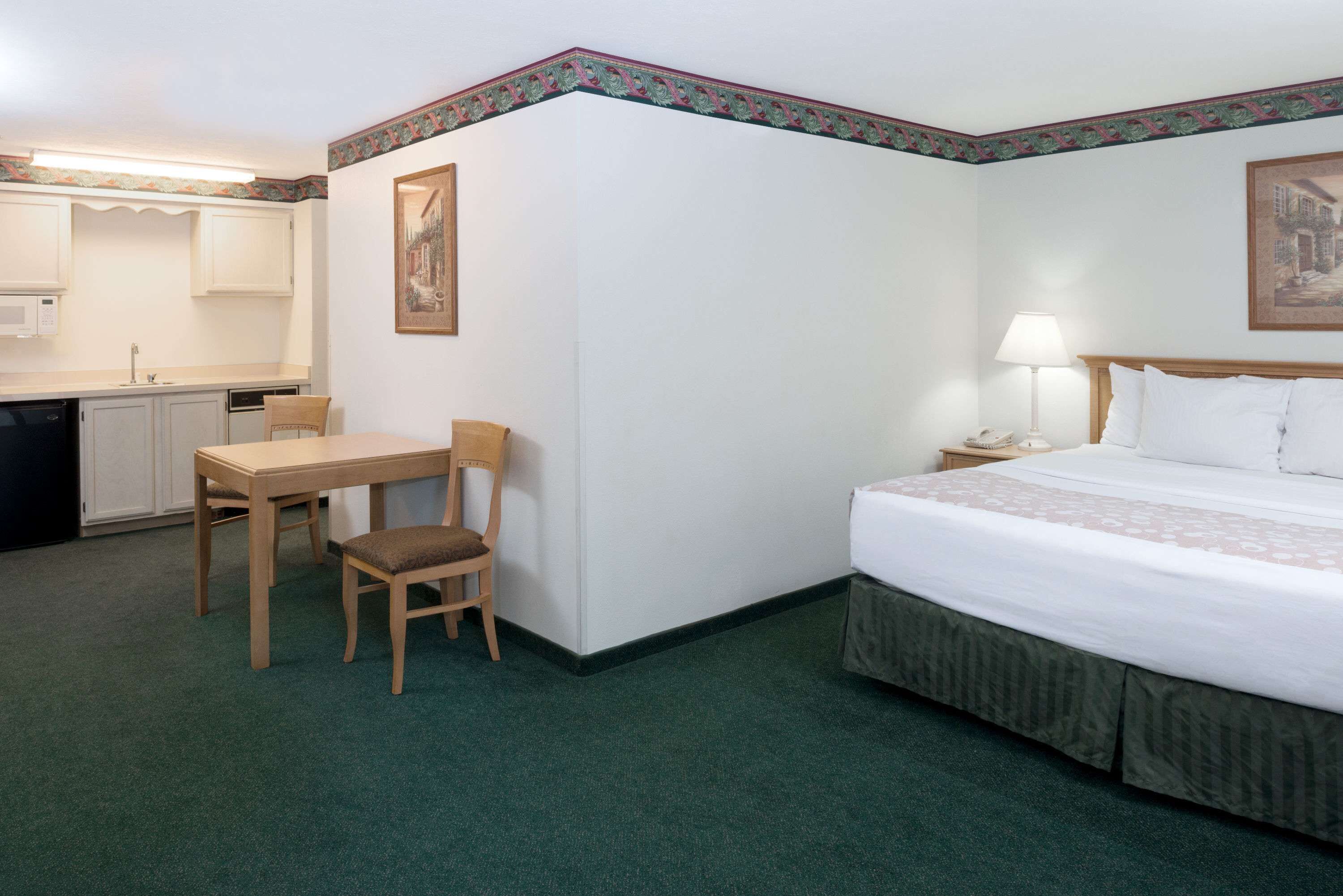 Una camera d'albergo con un letto, una scrivania, una sedia, una lampada e un quadro appeso al muro.