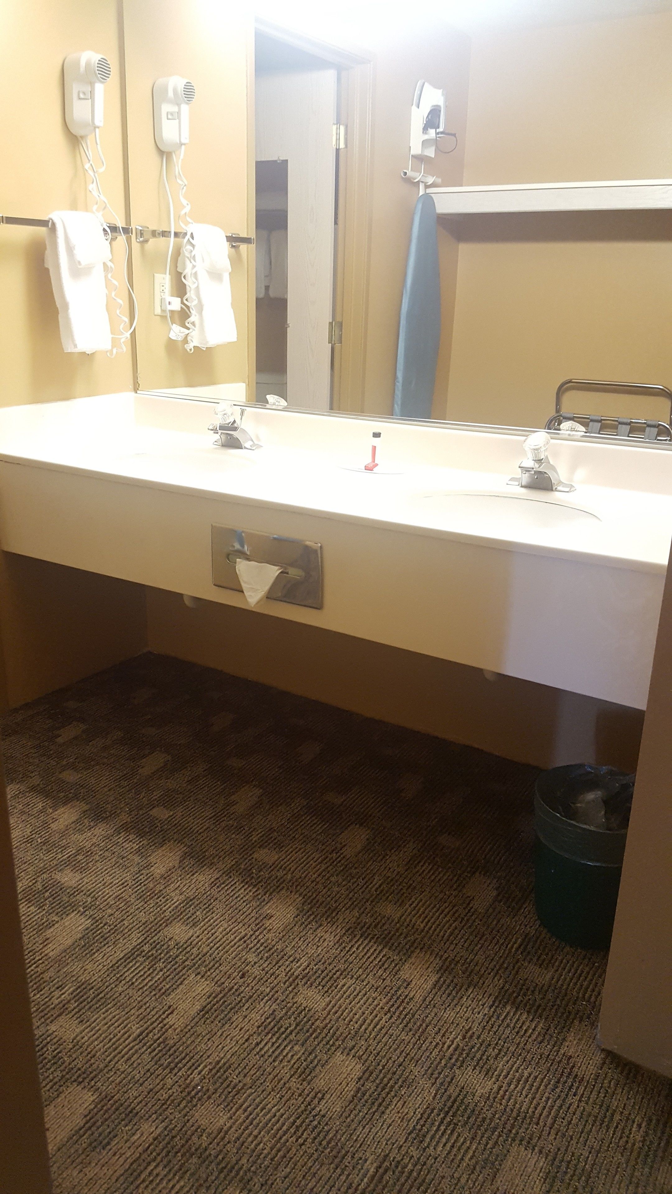 Un baño con un espejo grande, dos secadores de pelo, un lavabo y un perchero para toallas.