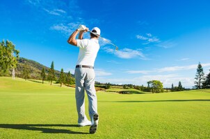 A person on a golf course with a clear sky and trees in the background.