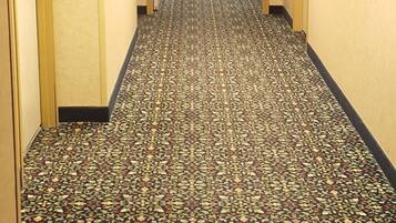 Un pasillo de hotel con pisos alfombrados, puertas a ambos lados y una señal de salida al final.