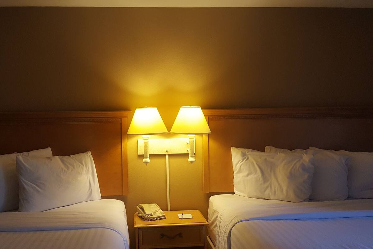 A hotel room with two beds, a nightstand with a telephone and notepad, and two wall-mounted lamps.