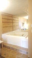 Un baño con una bañera grande, un revestimiento de pared de madera y un espejo sobre el lavabo.