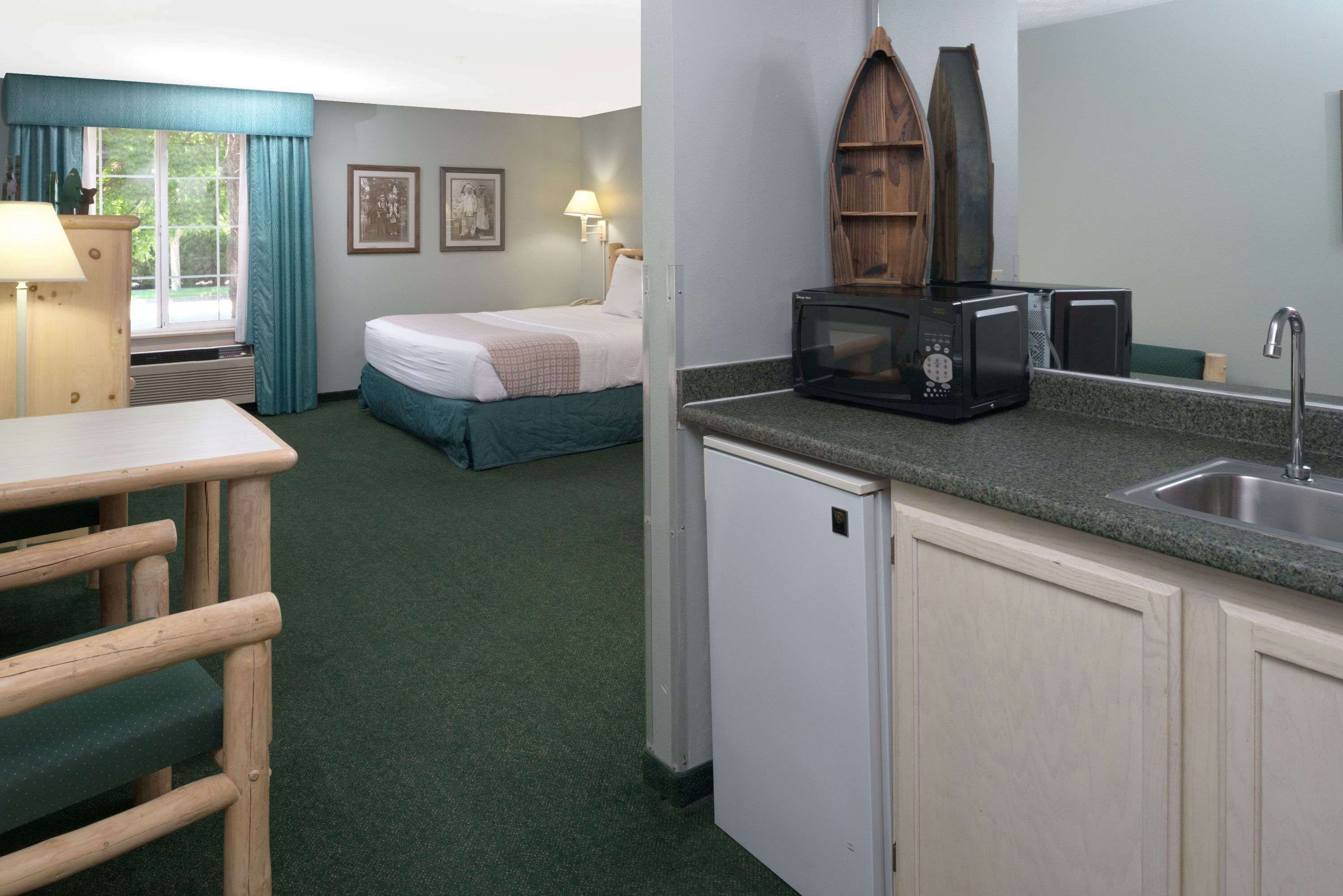A hotel room with a bed, a small kitchenette, a dining area, and a window with curtains.