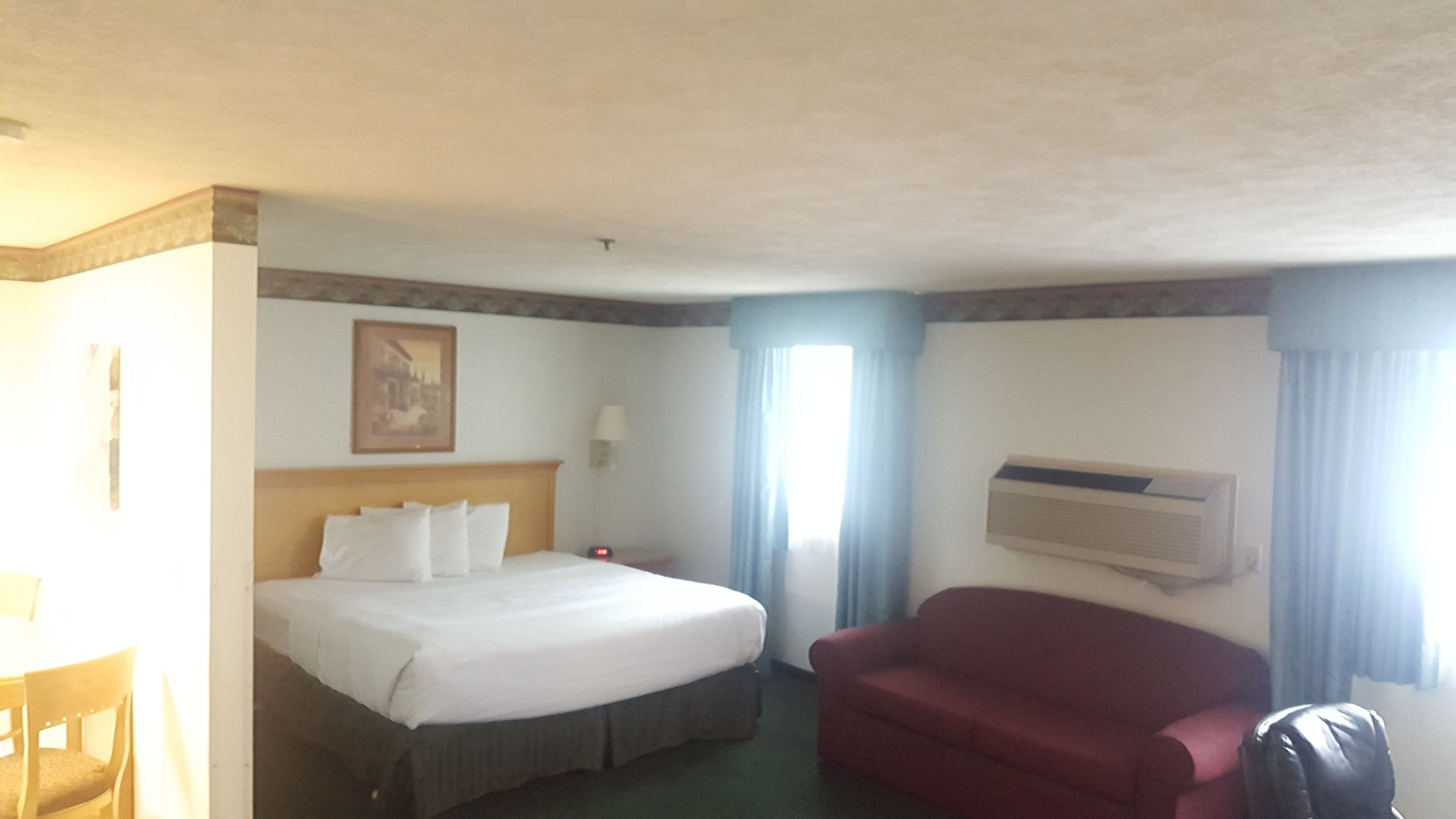 Hotellihuone, jossa on sänky, punainen sohva, työpöytä ja ilmastointilaite.