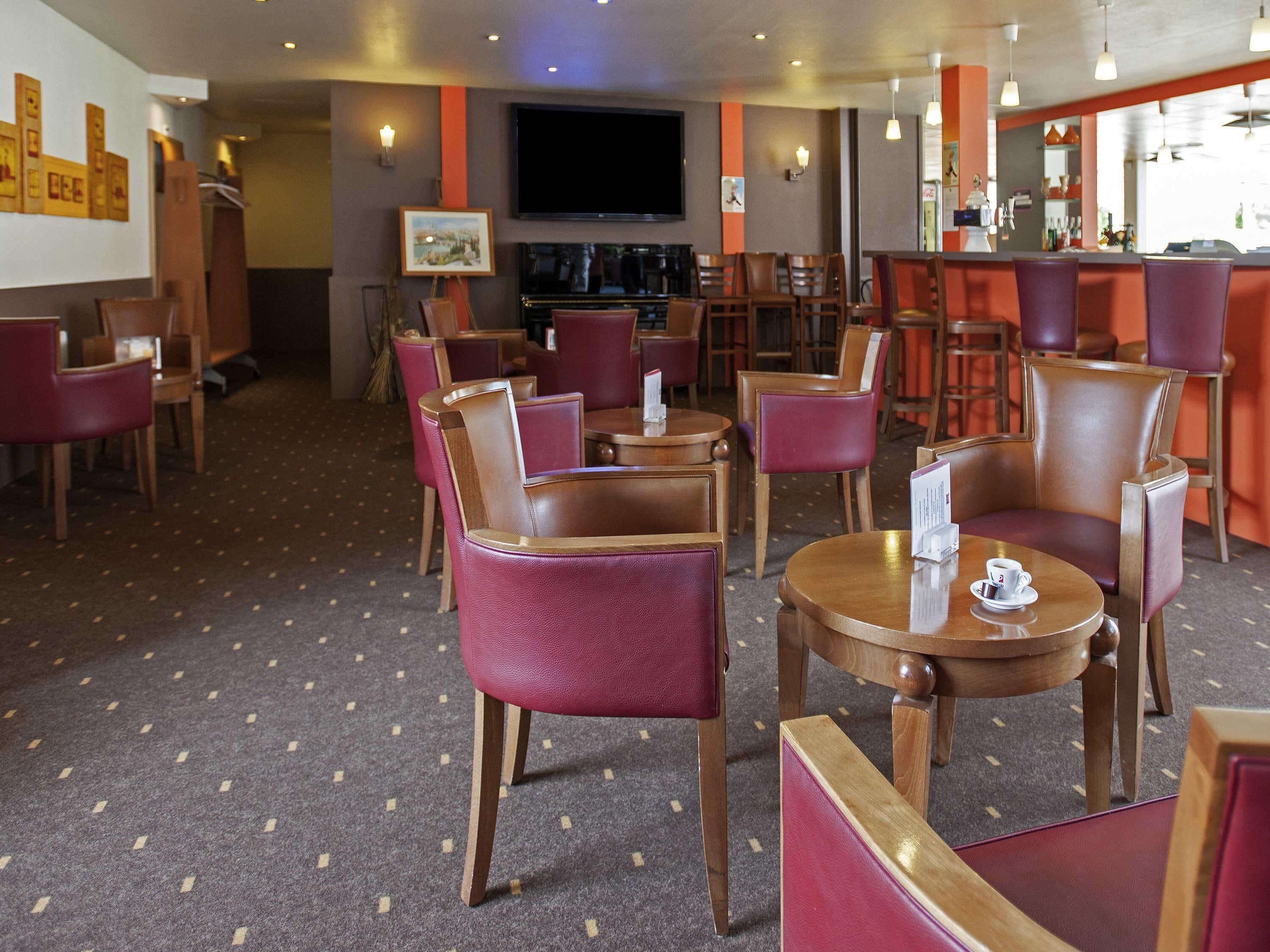 A hotel lobby with multiple seating areas, a bar, and a television screen.
