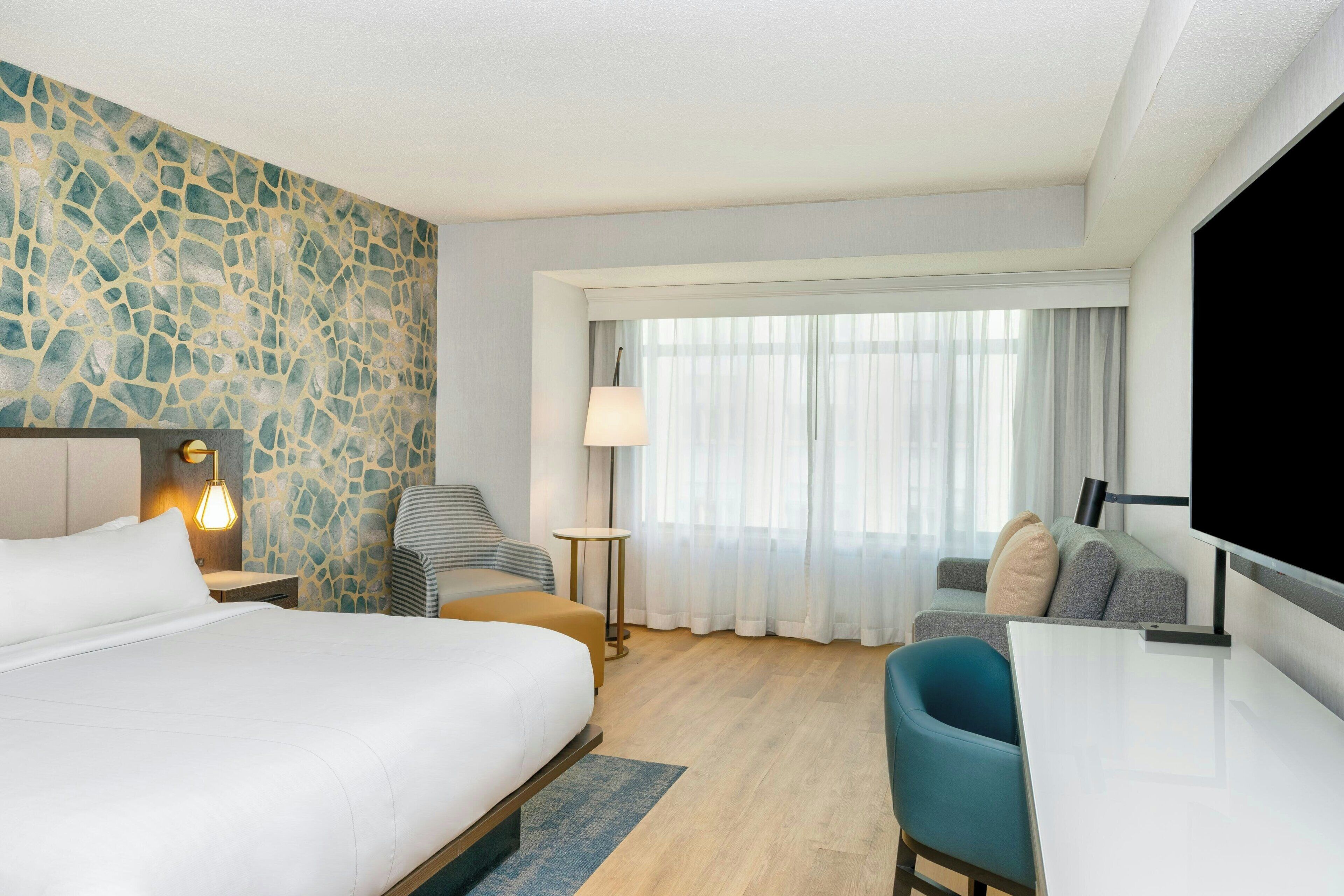 Een hotelkamer met een groot bed, een bureau, een stoel, een televisie en een raam met gordijnen.