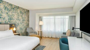 Een hotelkamer met een groot bed, een bureau, een stoel, een televisie en een raam met gordijnen.