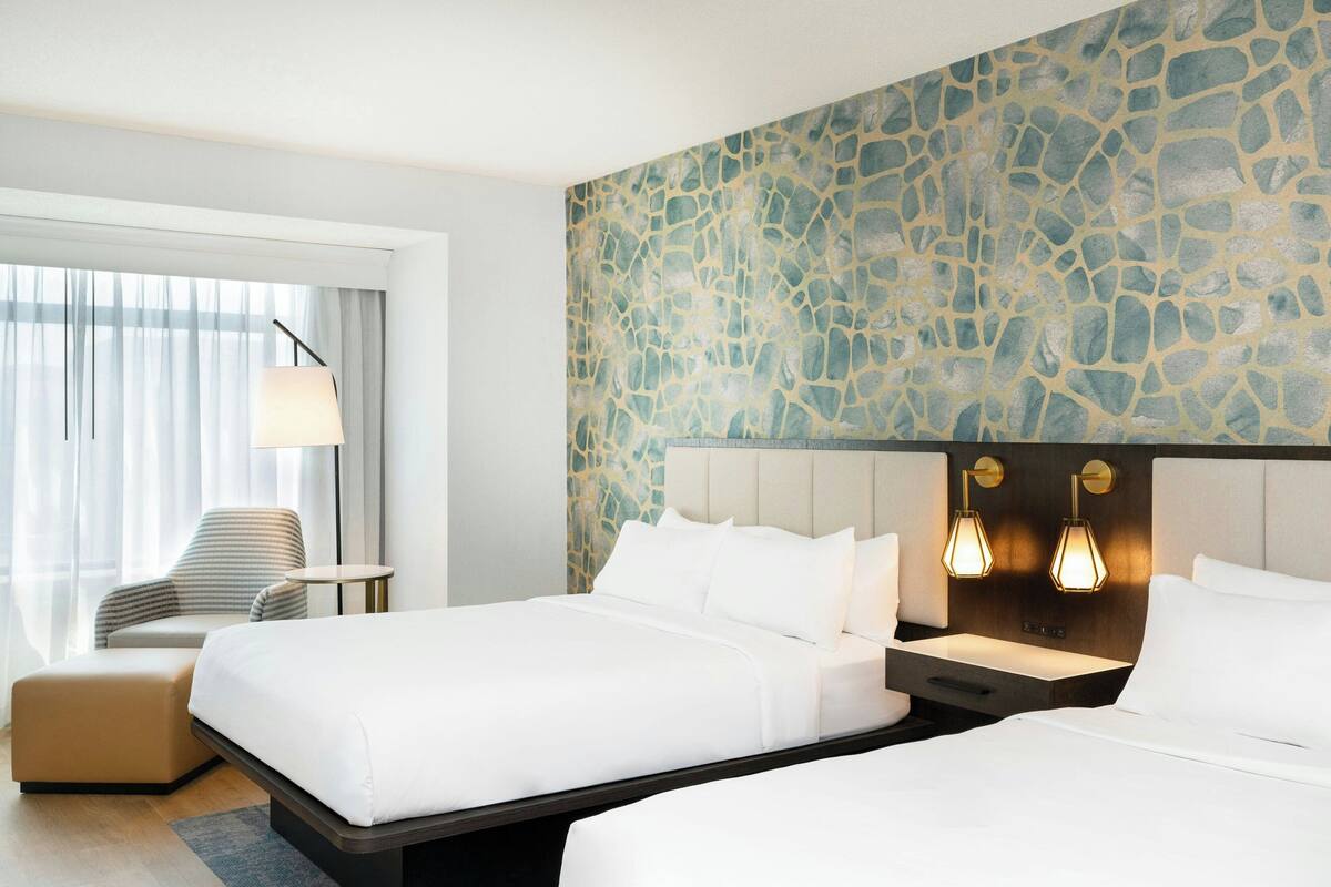 A hotel room with two beds, a sofa, a small table, and a stone-patterned wall.