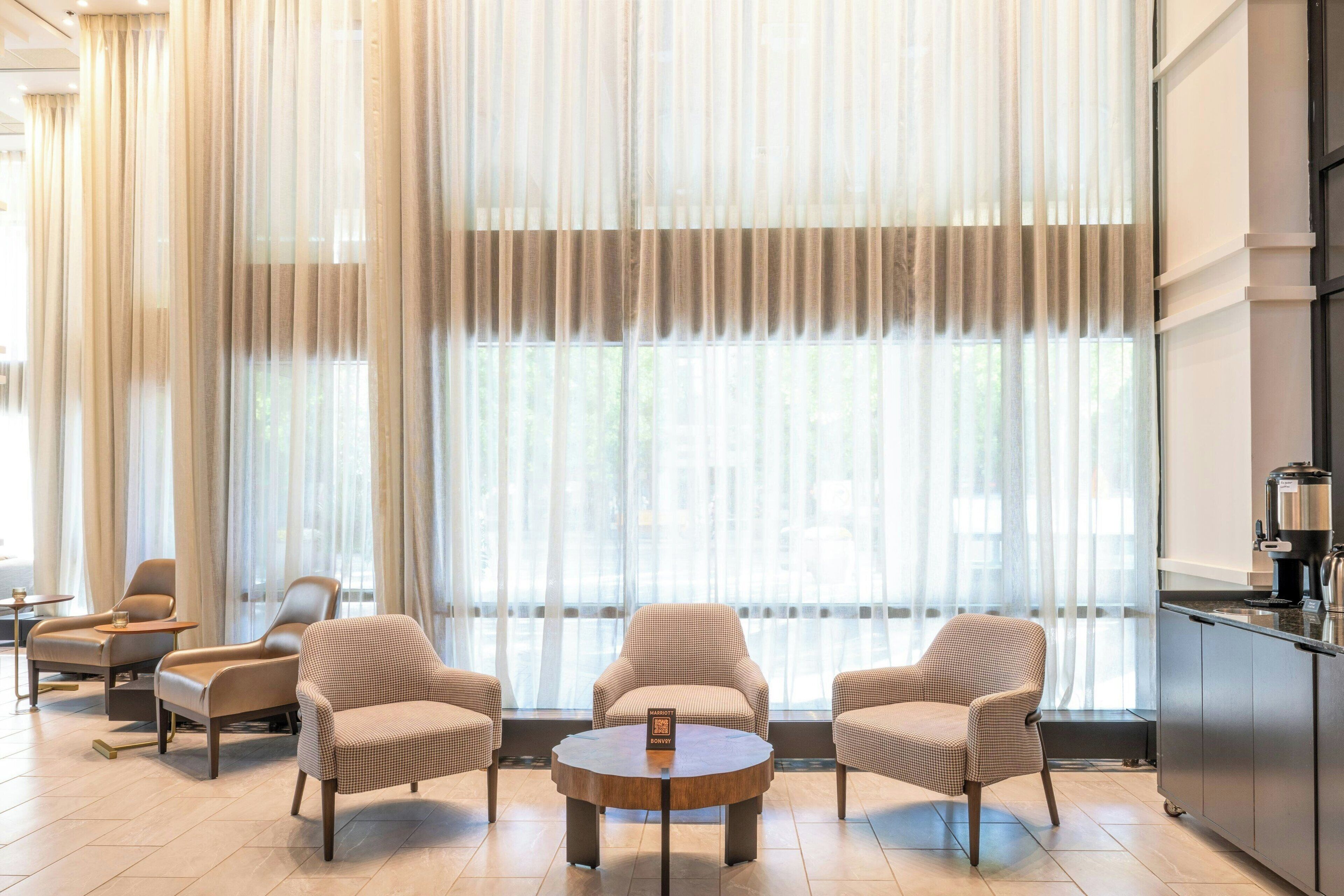 Un moderno vestíbulo de hotel con ventanas amplias, una mesa redonda para café y varias zonas de estar.