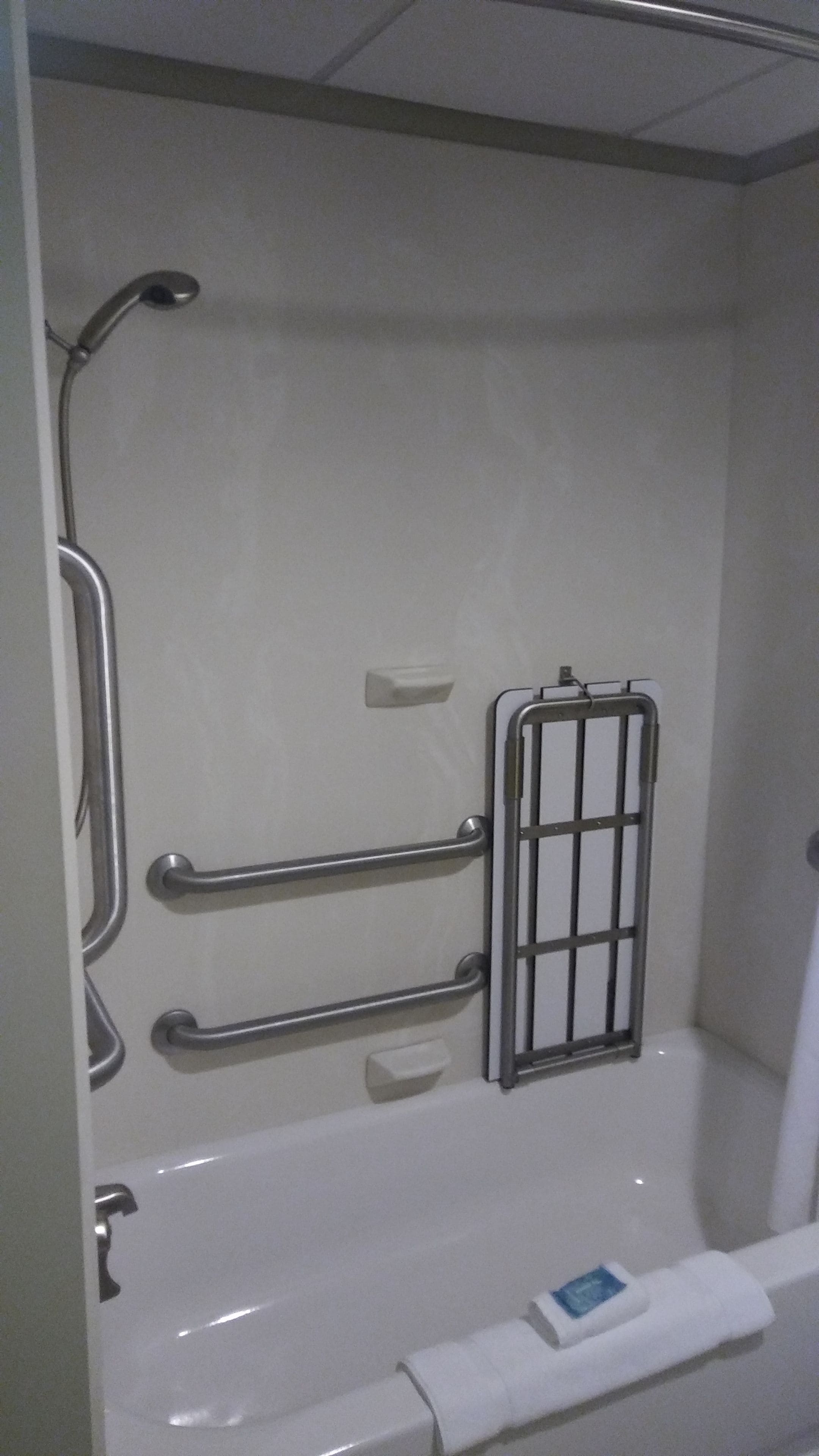 A bathroom with a bathtub, grab bars, and a towel dispenser.