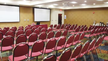 Una sala conferenze con file di sedie rosse, uno schermo per proiettore e un pavimento con moquette.