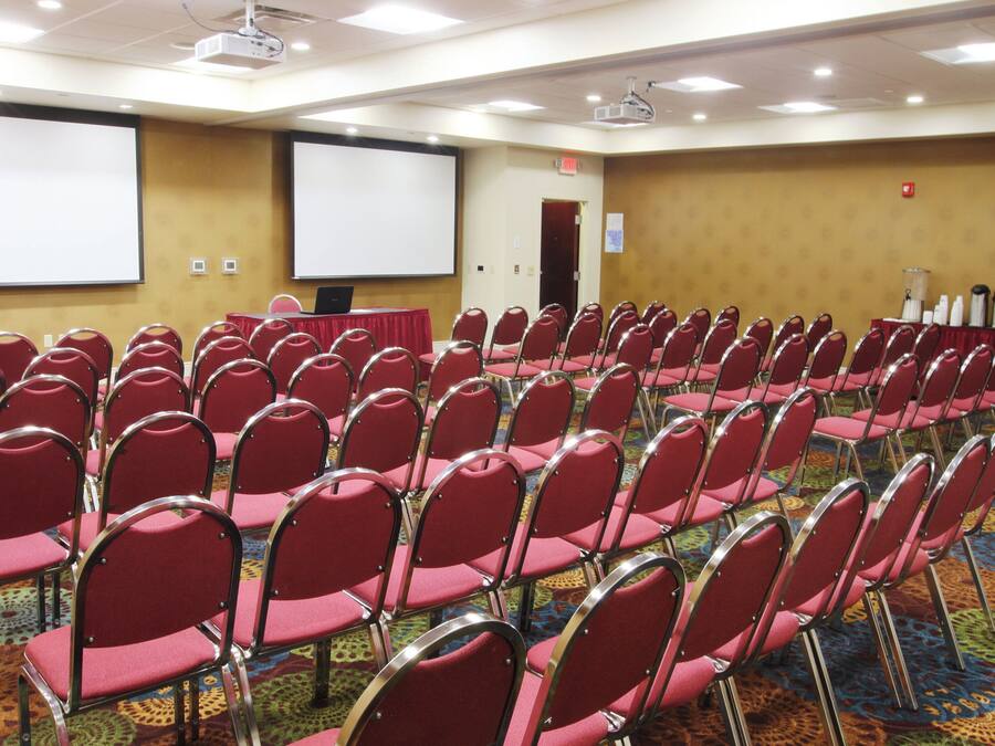 Una sala conferenze con file di sedie rosse, uno schermo per proiettore e un pavimento con moquette.