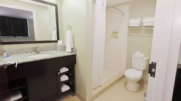 Un baño con lavamanos, espejo, toallero, cortina de ducha, inodoro y estante para toallas.