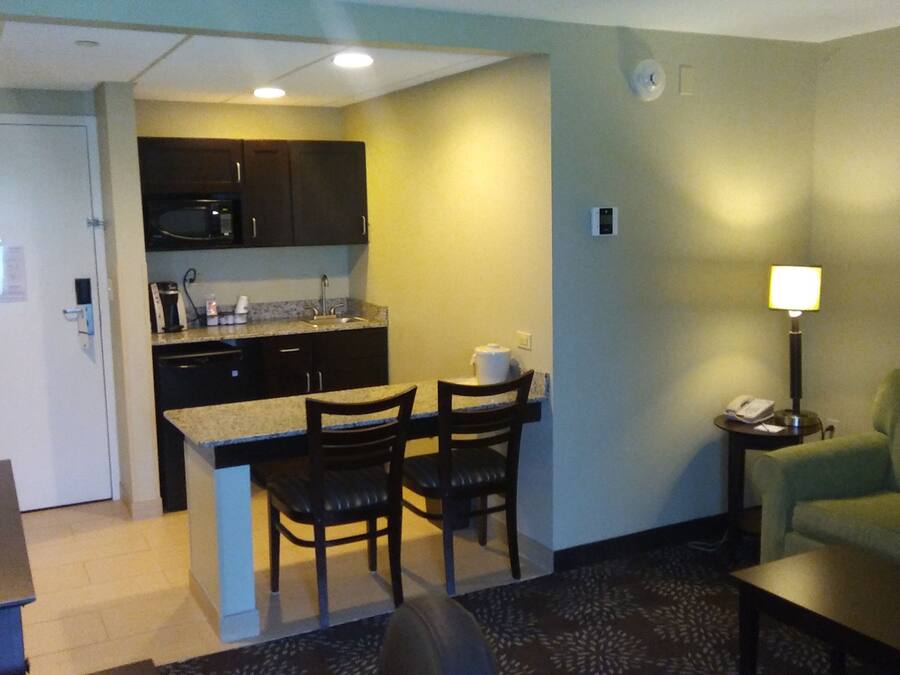 A compact hotel room with a kitchenette, a dining area with two chairs, a green sofa, and a small table.
