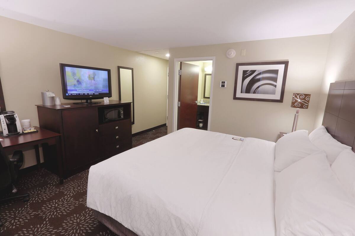 A hotel room with a bed, a desk with a television, a coffee maker, and a mirror.