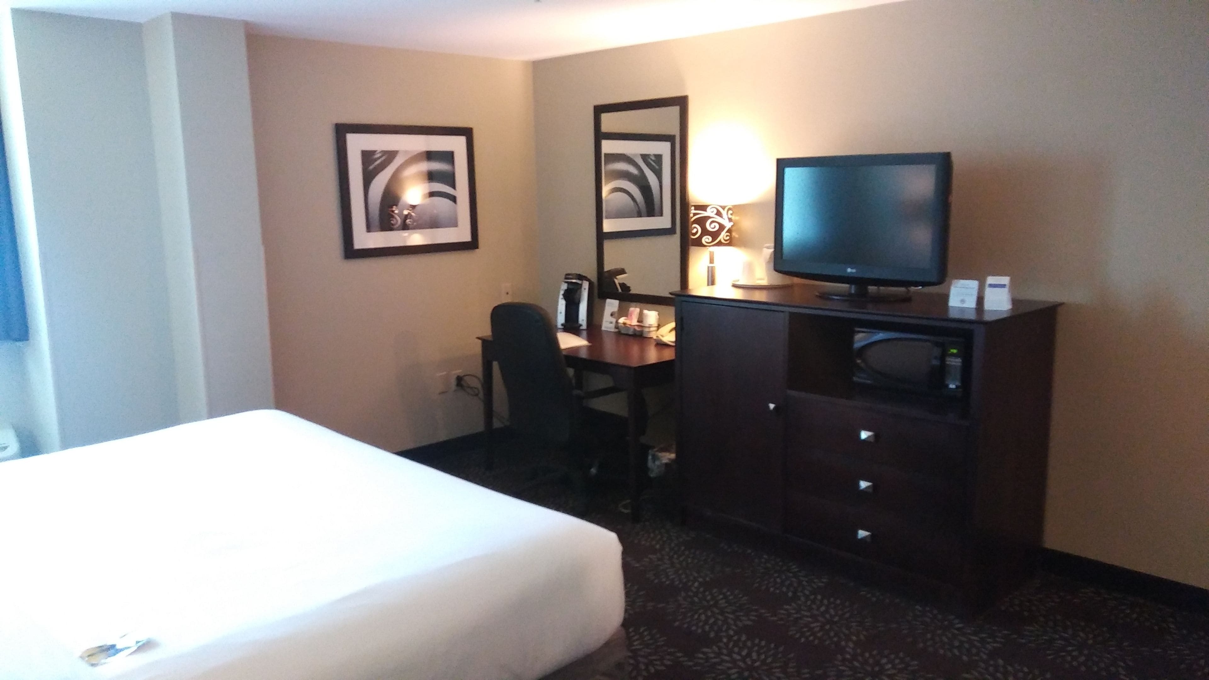 A hotel room with a bed, a desk with a computer, a television, and two framed pictures on the wall.