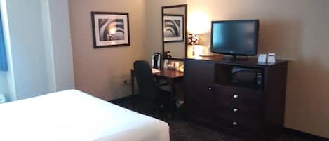 A hotel room with a bed, a desk with a computer, a television, and two framed pictures on the wall.