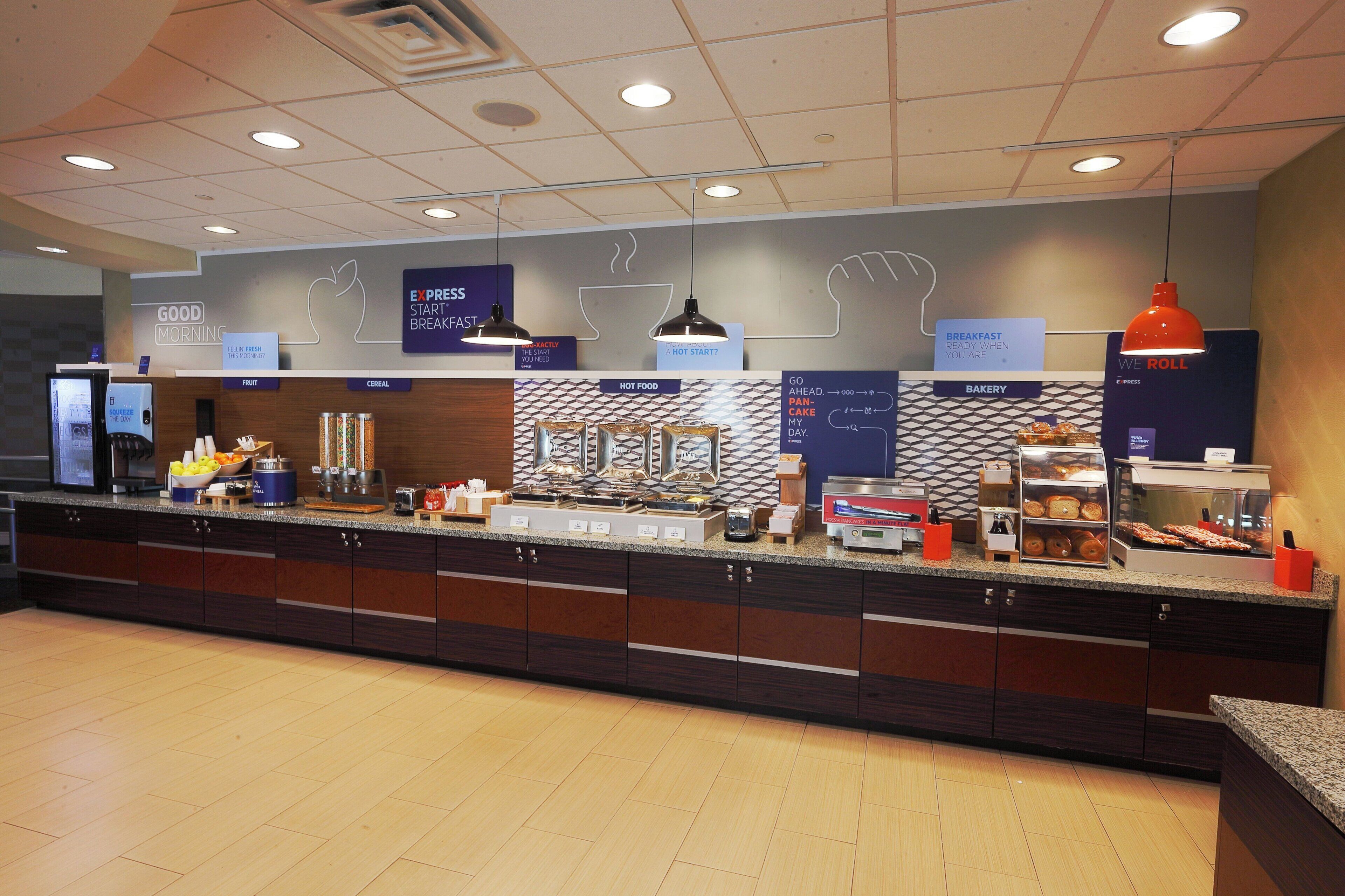 Zona de desayuno buffet con distintas estaciones de comida, que incluyen cereales, fruta, alimentos calientes y productos de panadería.