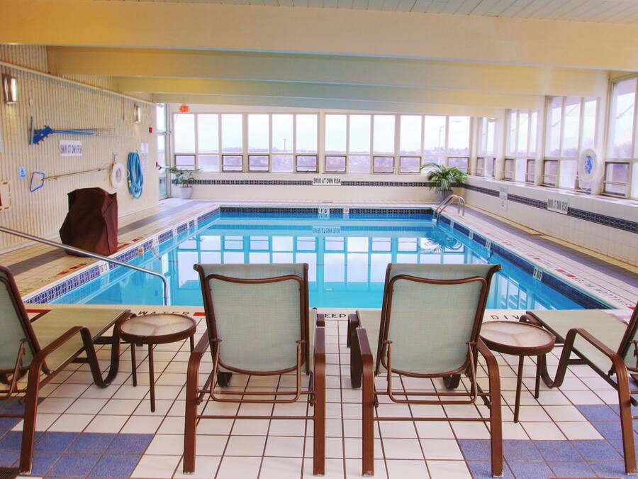 An indoor swimming pool with clear glass walls, multiple lanes, and a seating area with chairs.