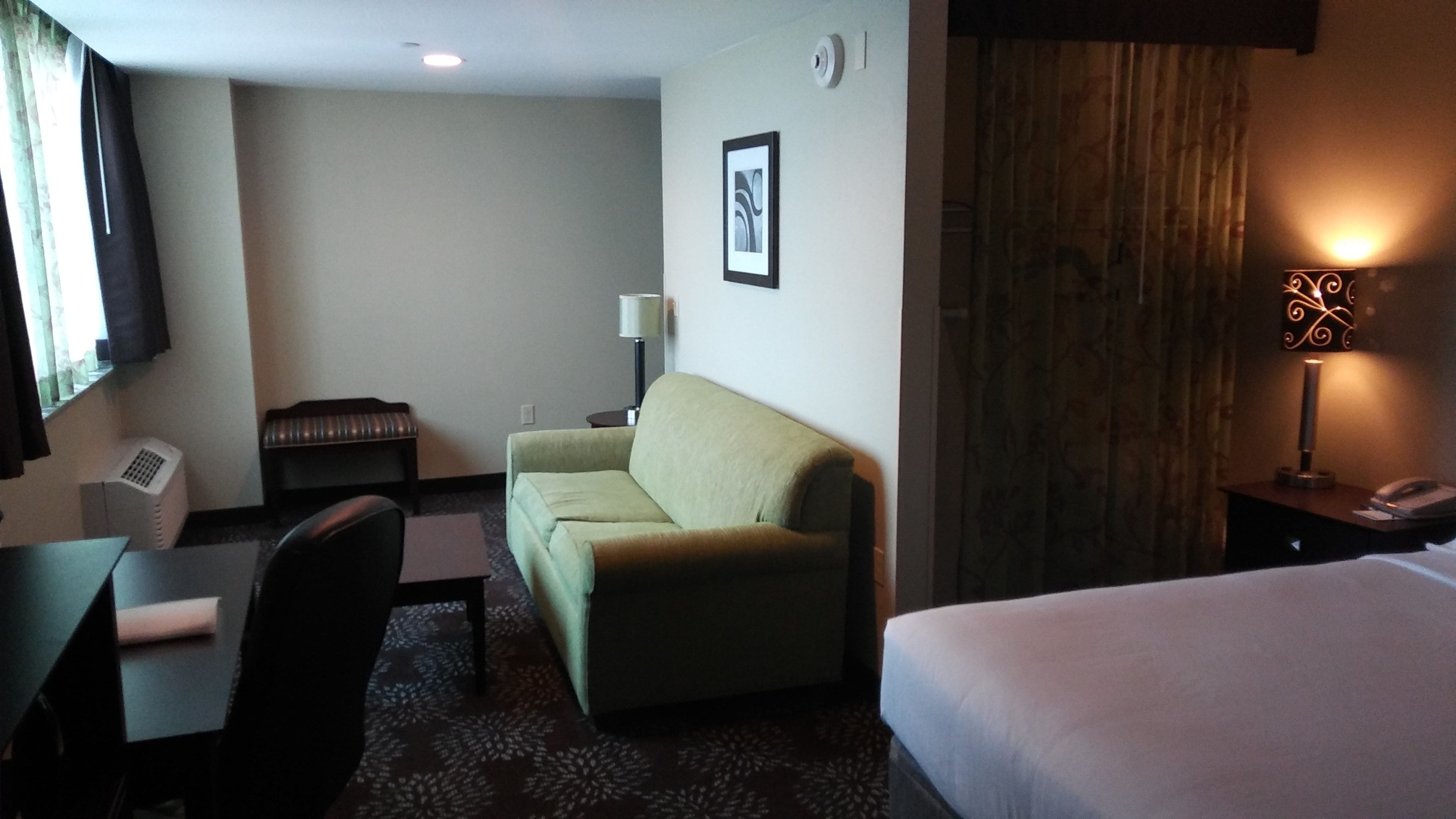 Une chambre d’hôtel avec un lit, un canapé, un bureau avec une chaise, une lampe et un tableau au mur.