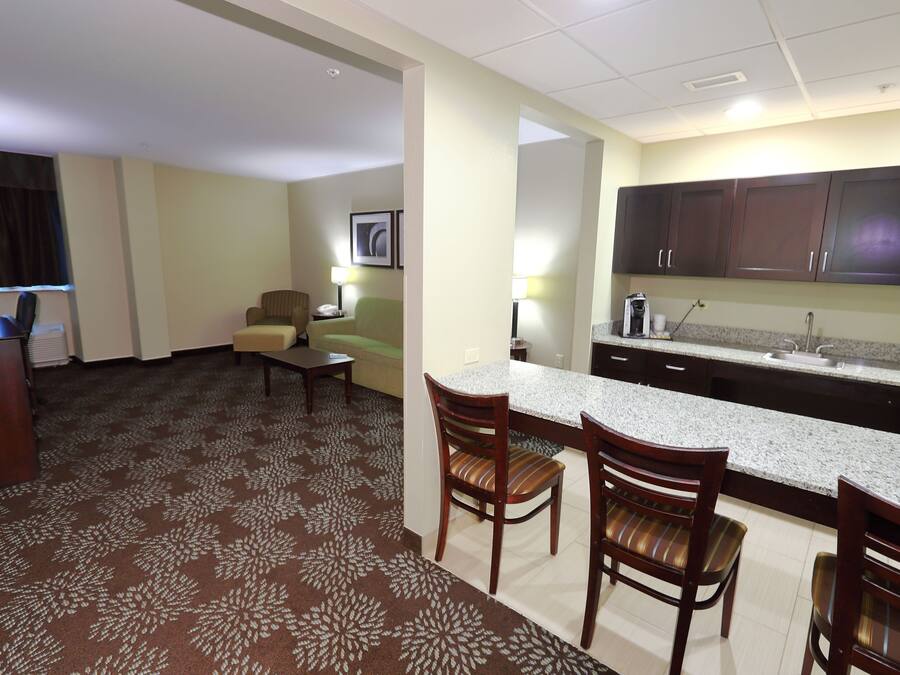 Habitación de hotel con kitchenette, zona de comedor con dos sillas, sofá, escritorio y lámpara.