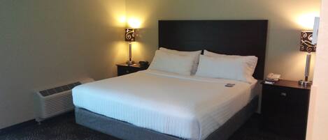 A hotel room with a large bed, two bedside tables with lamps, a heater, and a patterned carpet.