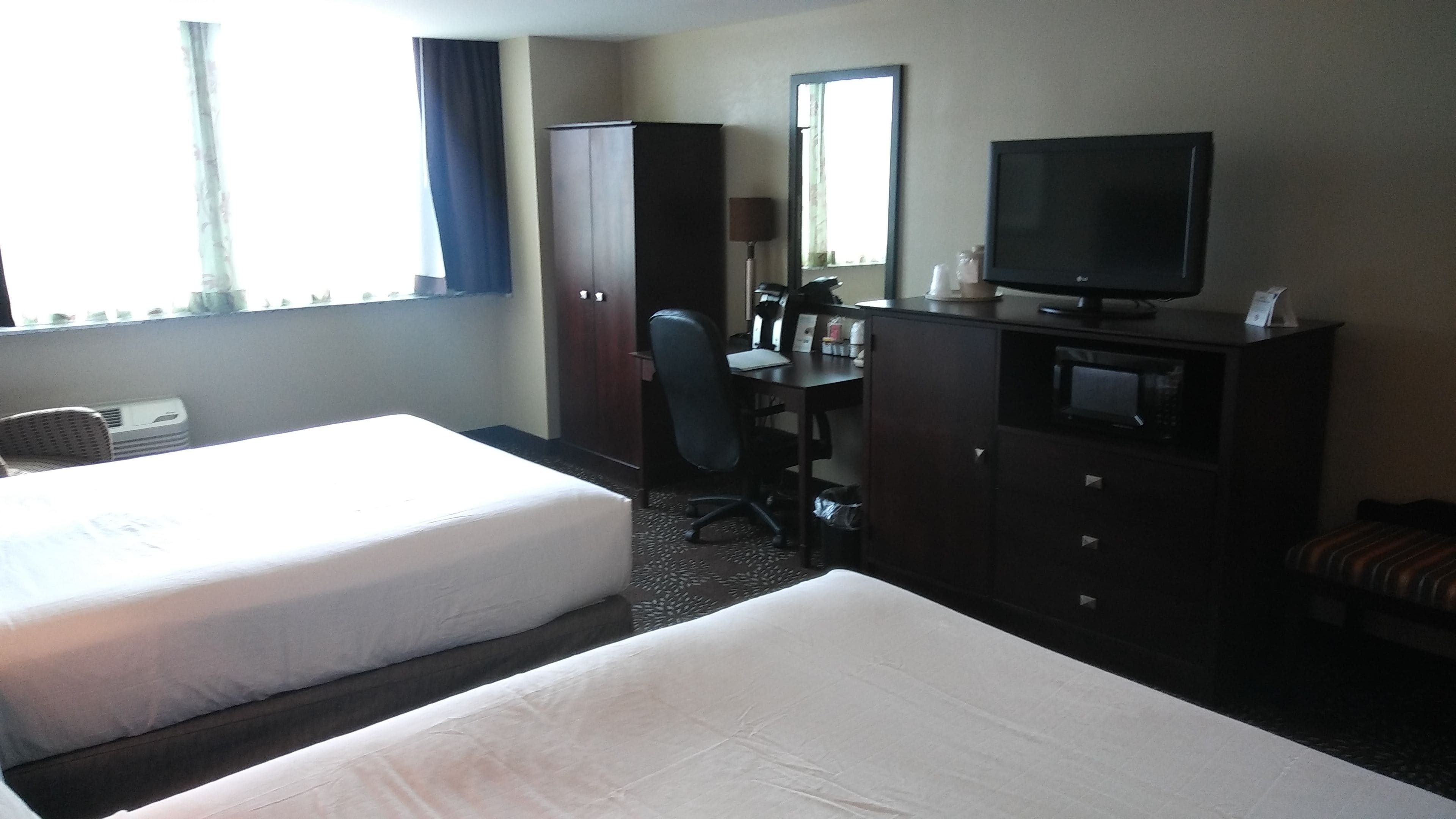 Una habitación de hotel con dos camas, un escritorio, una silla, un televisor y un armario.
