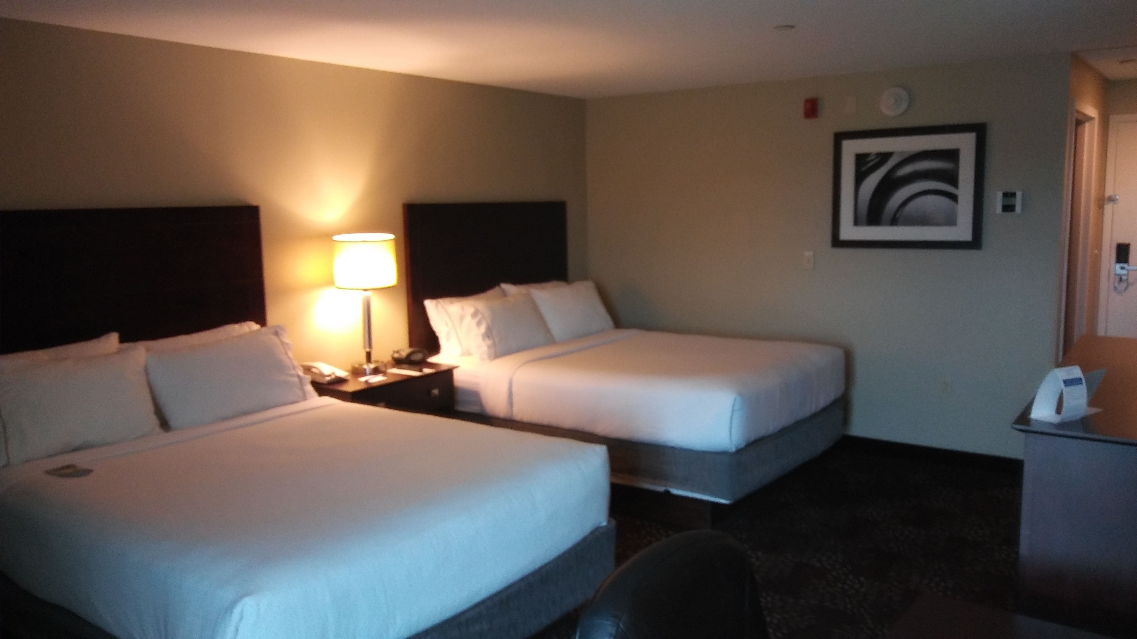 Quarto de hotel com duas camas, uma mesa de cabeceira com abajur, uma escrivaninha com telefone e um quadro pendurado na parede.