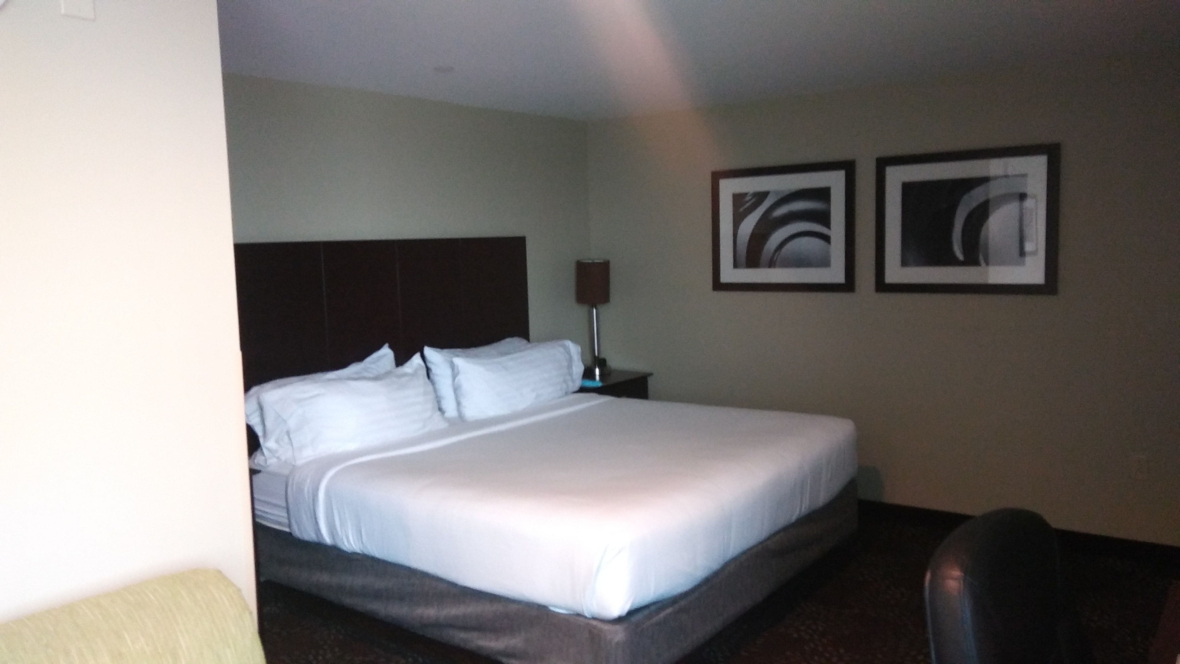 A hotel room with a large bed, a nightstand with a lamp, and two framed pictures on the wall.