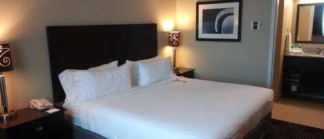 A hotel room with a large bed, a bedside table with a lamp, a framed picture on the wall, and a bathroom visible through an open door.