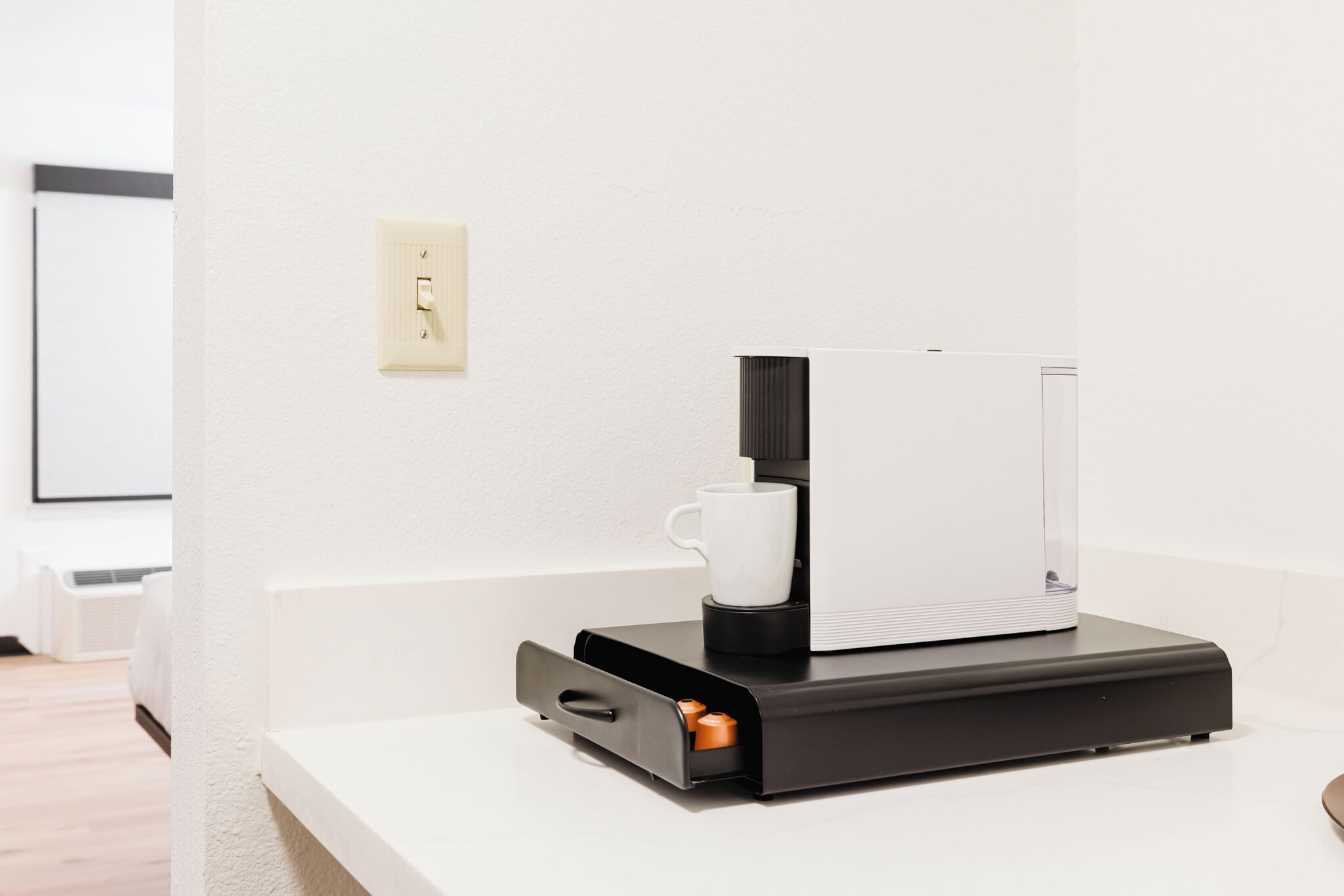 A coffee machine on a white countertop with a white mug beside it.