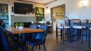 A modern restaurant interior with a wooden table, black chairs, and a bar area.