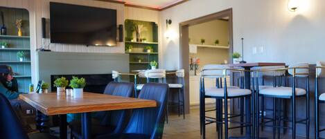 A modern restaurant interior with a wooden table, black chairs, and a bar area.
