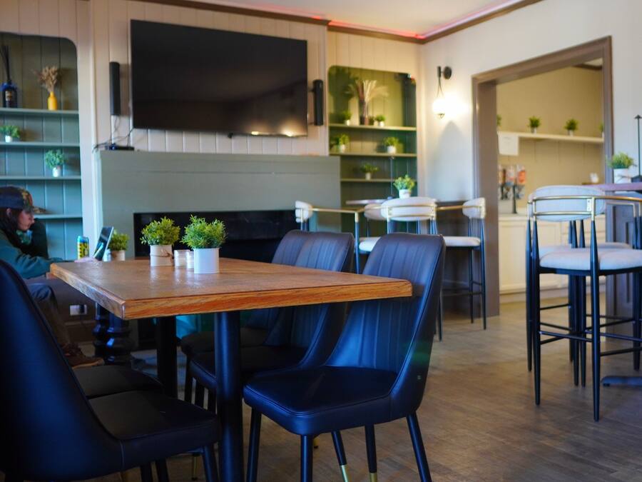 Un interior de restaurante moderno con una mesa de madera, sillas negras y una zona de bar.