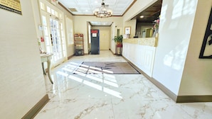 A hotel lobby with a marble floor, a reception desk, and a door leading to the interior.