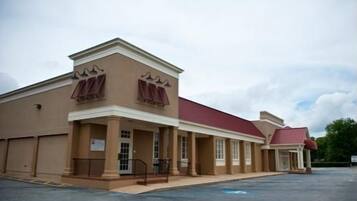 A two-story building with a red roof and beige walls, featuring a covered entrance with columns and a small porch.