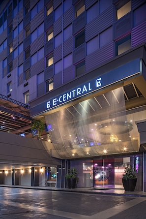 A hotel entrance with a modern facade, large potted plants, and a prominent sign.