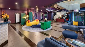 A modern lobby with a purple wall, a yellow sofa, and a blue couch.