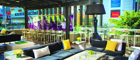 Un espacio lounge moderno con sofás, mesas y sillas, que ofrece vistas a la ciudad a través de amplios ventanales.