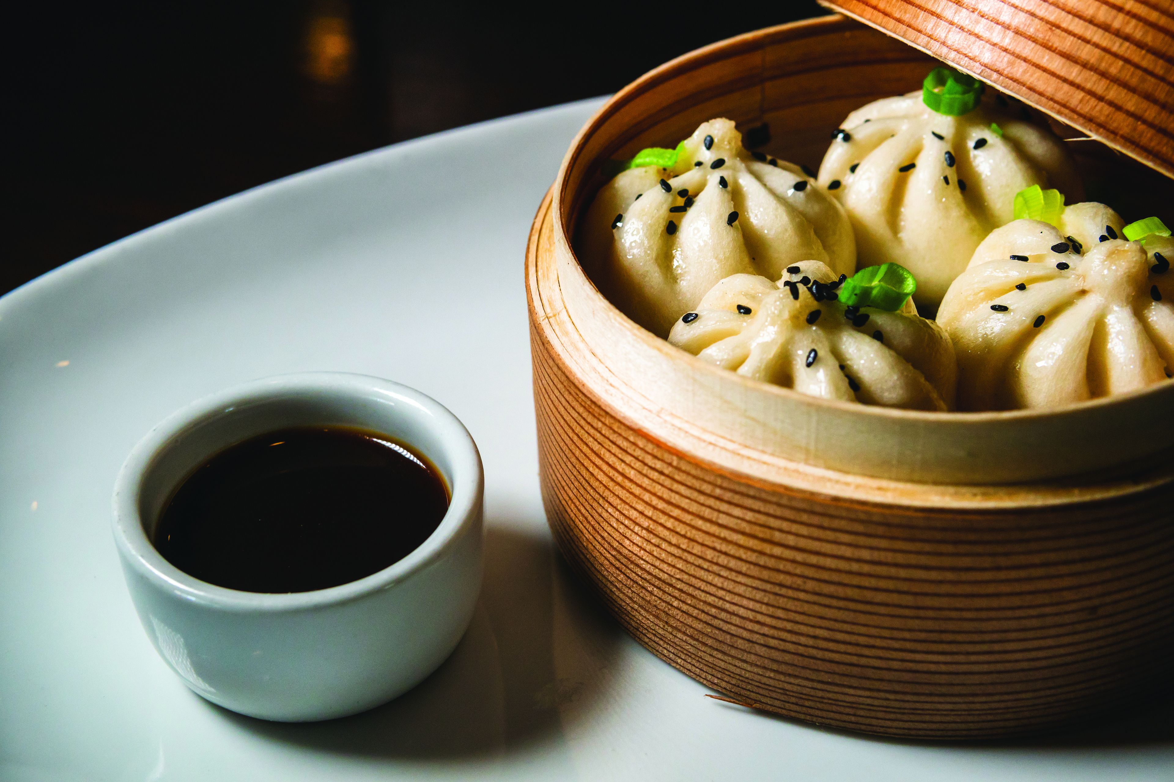 A bowl of dumplings with a small cup of soy sauce beside it.