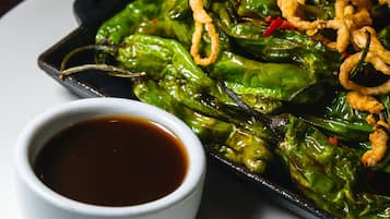 Un plat de poivrons verts grillés, accompagnés d’oignons frits et d’une petite portion de sauce.