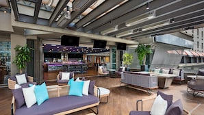 A rooftop lounge with wicker furniture, a bar area, and large windows.