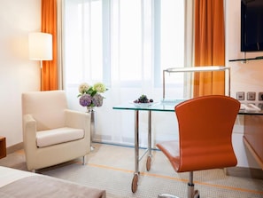 A hotel room with a bed, two chairs, a desk with a lamp, a vase with flowers, and a television. - Sunday am Main Taunus Zentrum Frankfurt/Sulzbach (Sulzbach)