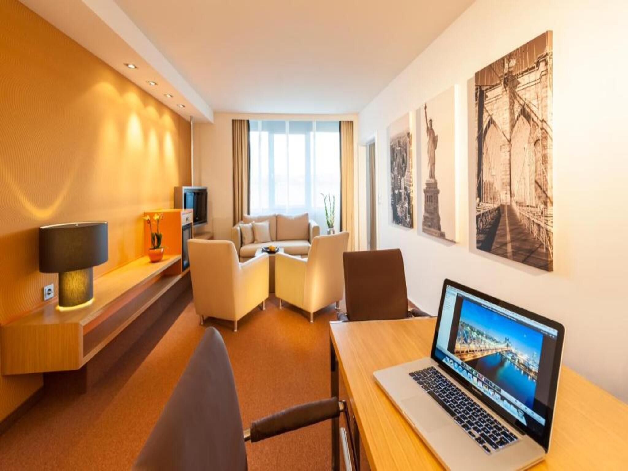 Habitación de hotel con escritorio, laptop, sofá y televisor.