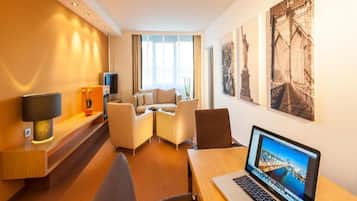 Habitación de hotel con escritorio, laptop, sofá y televisor.