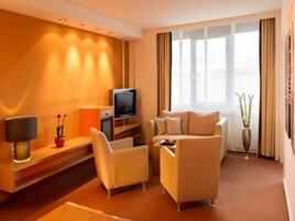 Habitación de hotel con sofá, sillones, televisor, lámpara, una mesita y una planta.