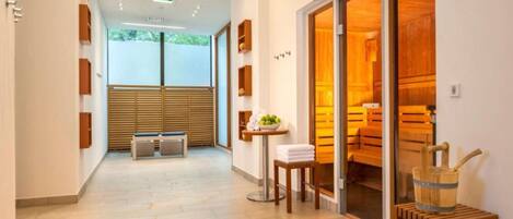 A hotel corridor with a wooden bench, a small table with towels, and a sauna visible through the glass doors.