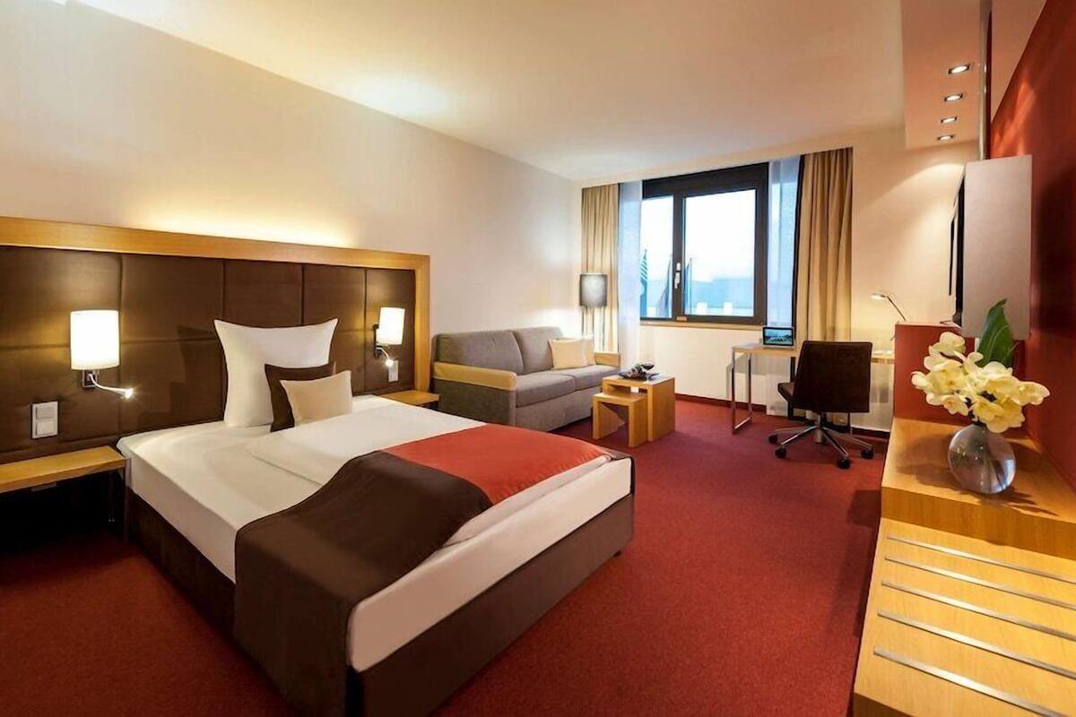 A hotel room with a large bed, a desk, a sofa, and a view of the city.