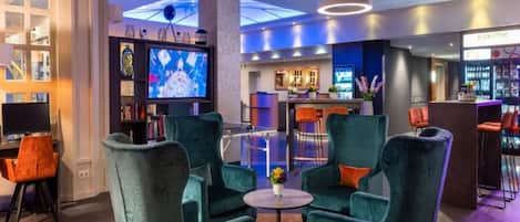 Un espacio de descanso moderno con sillones turquesa, una mesita redonda y una pantalla de televisión.